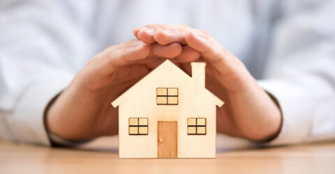 Image d'une personne positionnant ses mains au-dessus d'une maison en papier pour la protéger