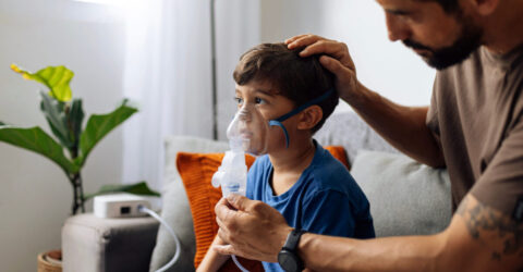 Père aidant un jeune enfant lors d’une thérapie par nébuliseur à domicile, illustrant les soins parentaux, le traitement respiratoire pédiatrique et le soutien émotionnel familial